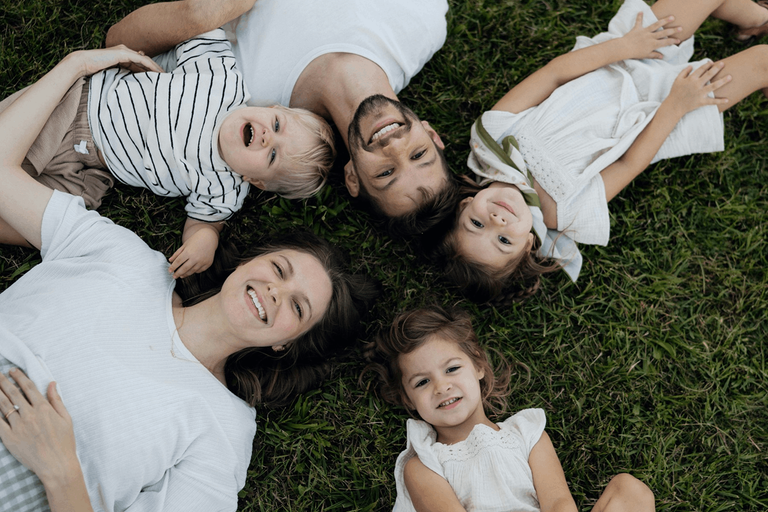 A mom lying on the grass with her three young children, all smiling up at the camera